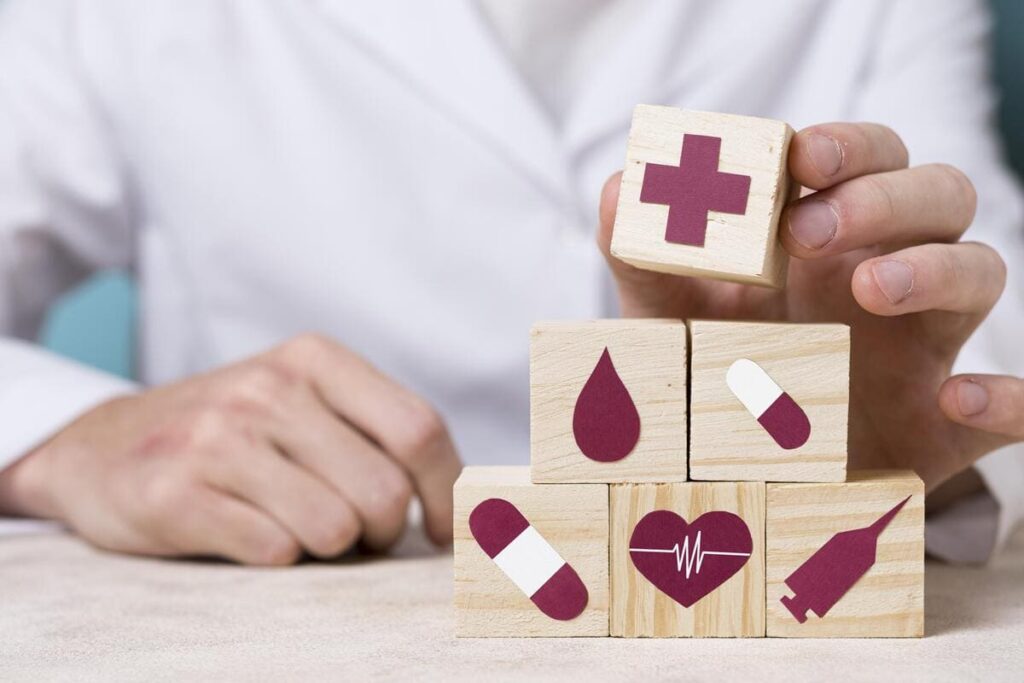 Médico empilhando blocos de madeira com ilustrações de ícones referentes à medicina, em alusão aos planos de saúde coletivos por adesão.