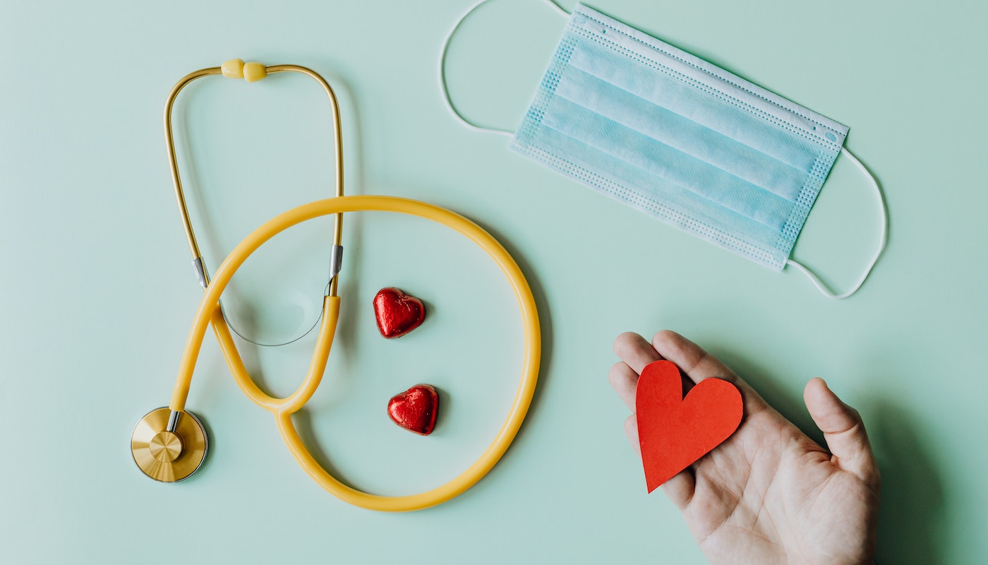 Na imagem, observamos um medidor de frequência cardíaca, uma máscara descartável e corações de papel