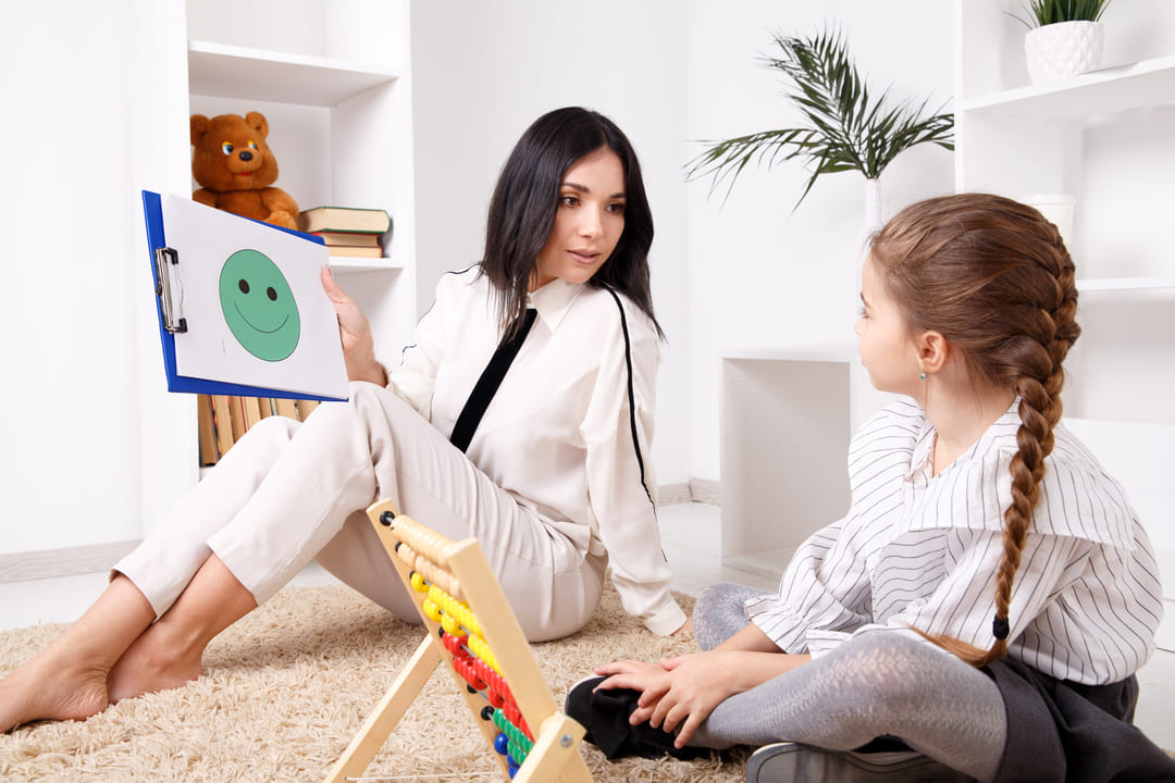 Terapia Infantil: uma psicologa mostrando um emoji feliz para uma criança.