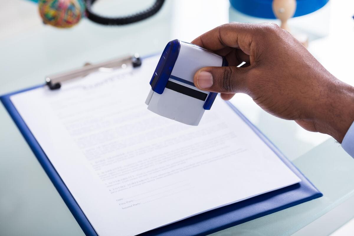 Mão de profissional da saúde carimbando documentos médicos para a autorização de exames.